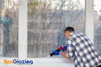 Man sealing a window frame with caulking for insulation and glazing work.